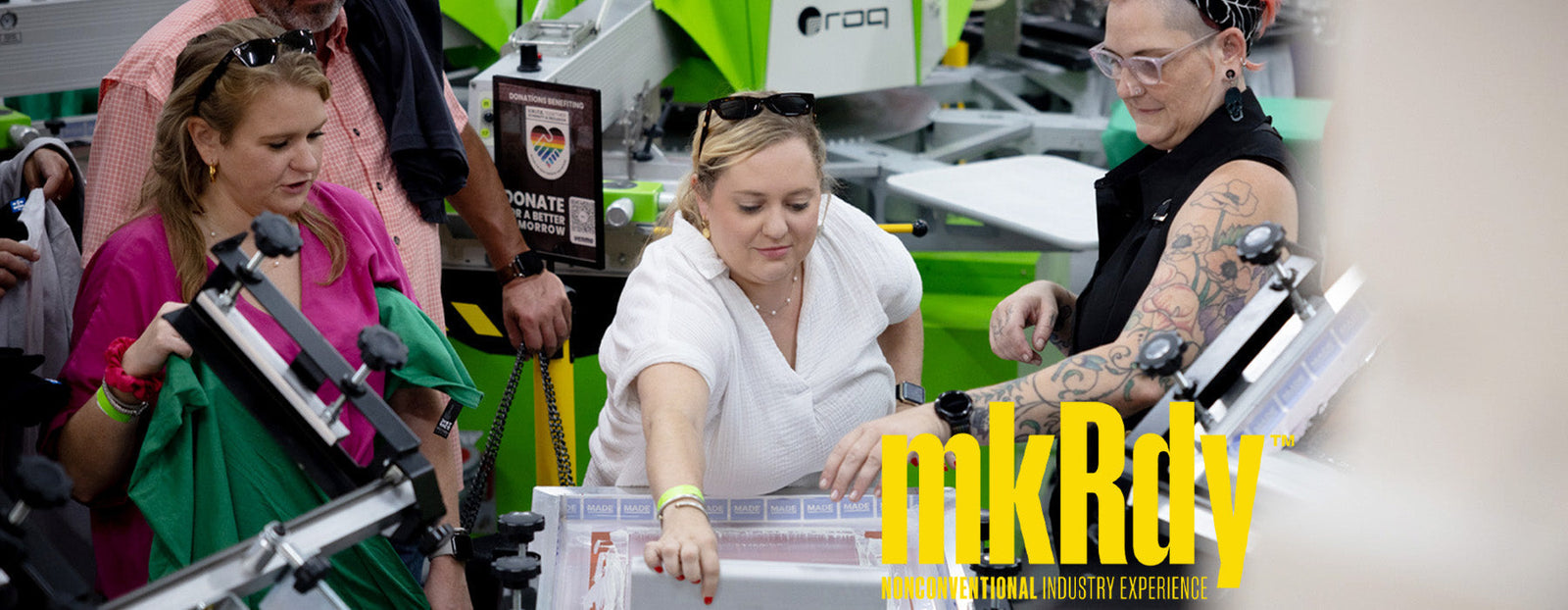 People printing on a Riley Hopkins press with ROQ Autos in the background.