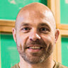 Jay D., owner of Threaded Ink screen printing and embroidery shop, smiling in front of green screen printing frames.