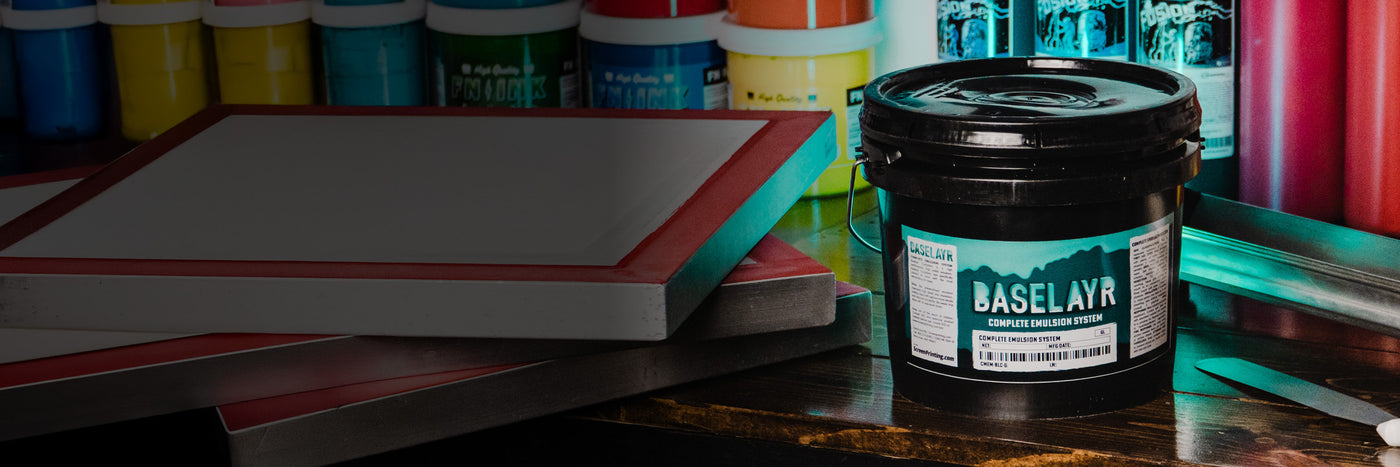 Baselayr complete emulsion system with coated screens and vibrant FN-INK and Green Galaxy screen printing inks on a workbench in a professional darkroom setup.