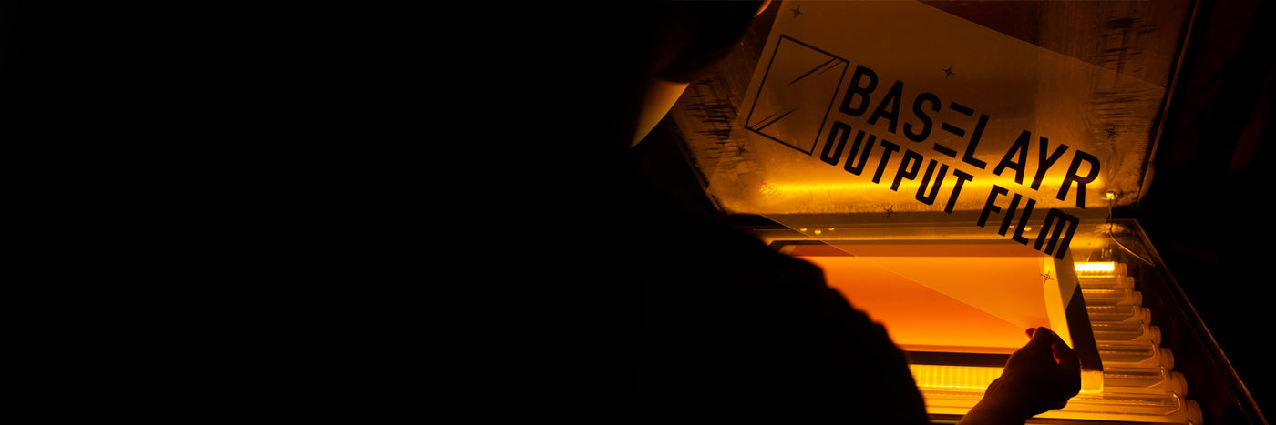 Printer holding Baselayr Output Film under yellow-orange safe light of exposure unit in darkroom.