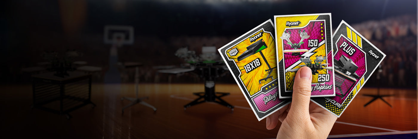 Hand holds three Ryonet “Machine Madness” trading cards featuring a flash dryer, Riley 150/250 presses, and a tabletop conveyor dryer, over a blurred basketball arena.