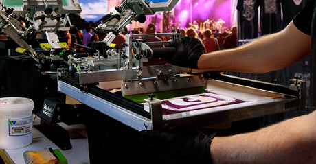 Close-up of custom t-shirt production at a live event using a Riley Hopkins 250 manual screen printing press with a Rudy Press attachment.